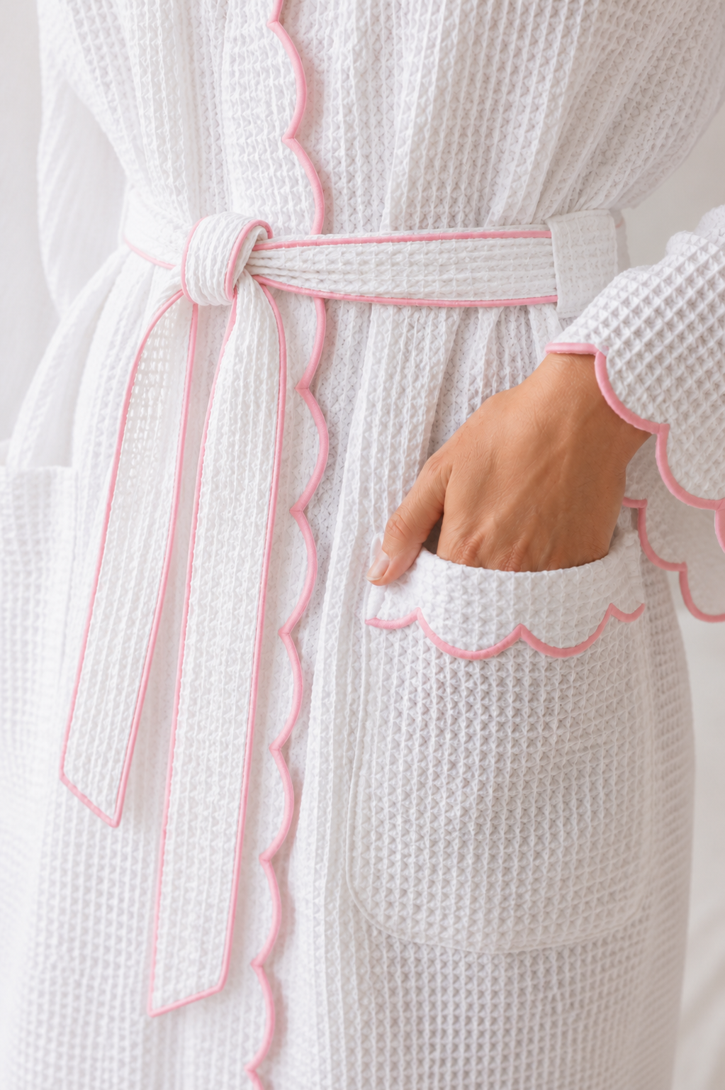 White textured robe with pink trim and a hand in the pocket against a light background