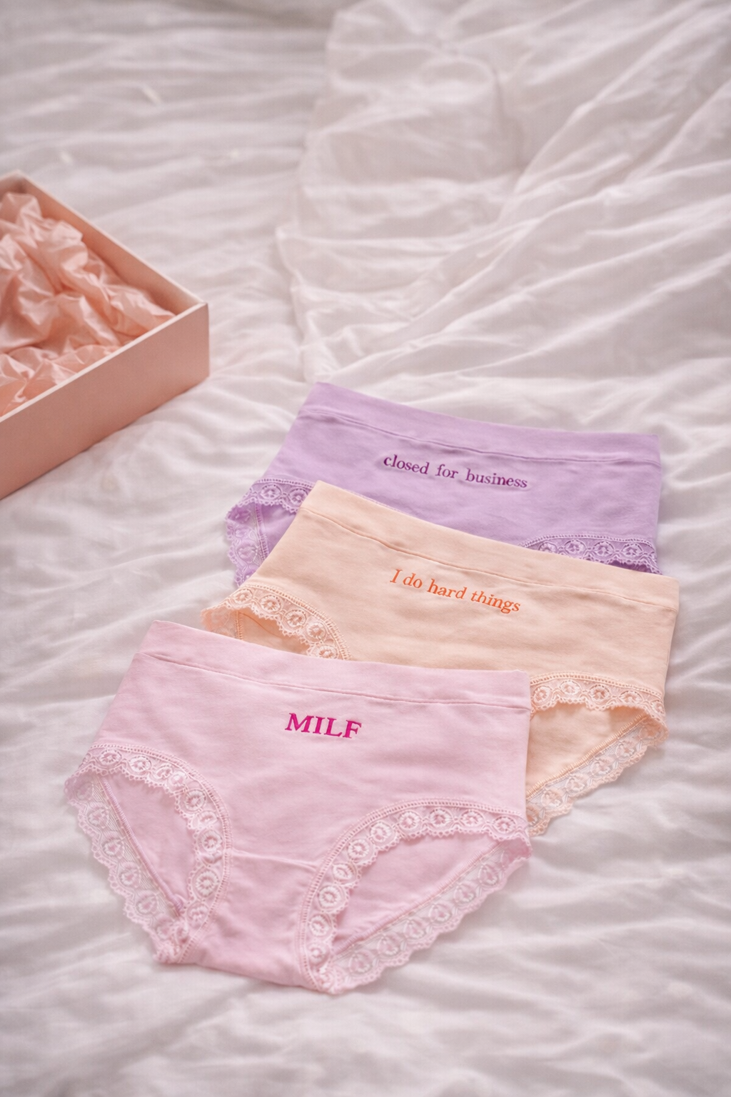 Three pairs of pastel-colored underwear with lace details on a textured surface.