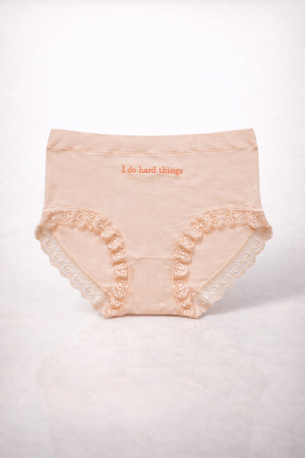 Beige lace-trimmed underwear with 'I do hard things' text on a white background