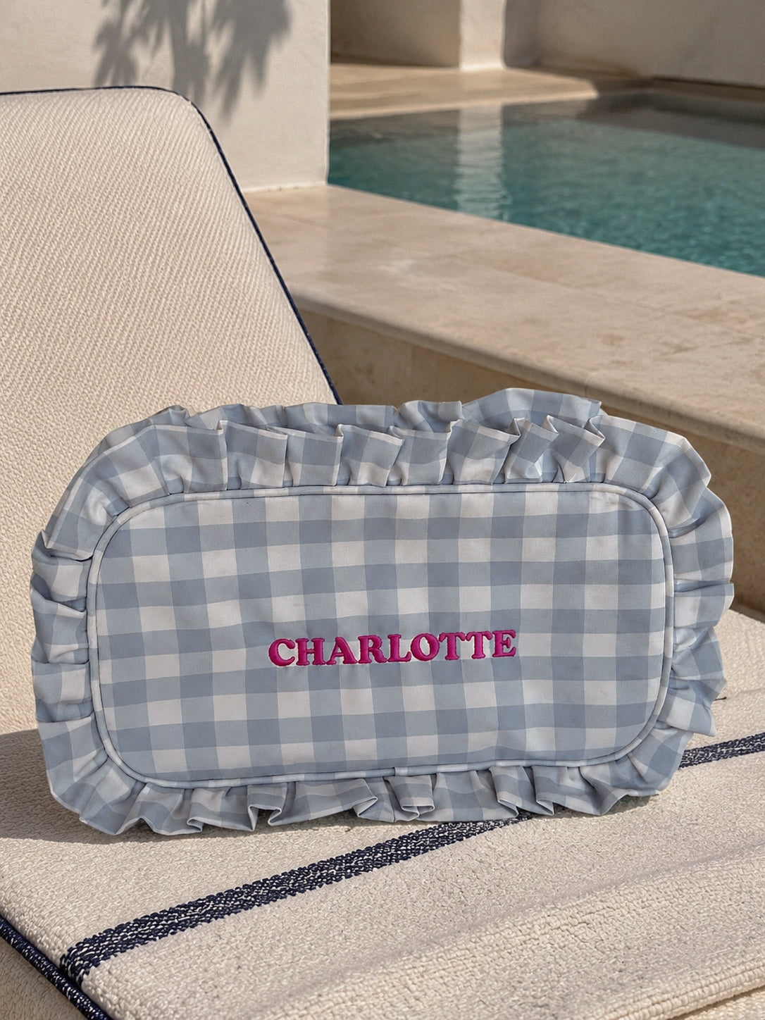 A personalized washrag featuring a light blue and white gingham check pattern with a ruffled border. The name 'CHARLOTTE' is embroidered in pink across the center.
