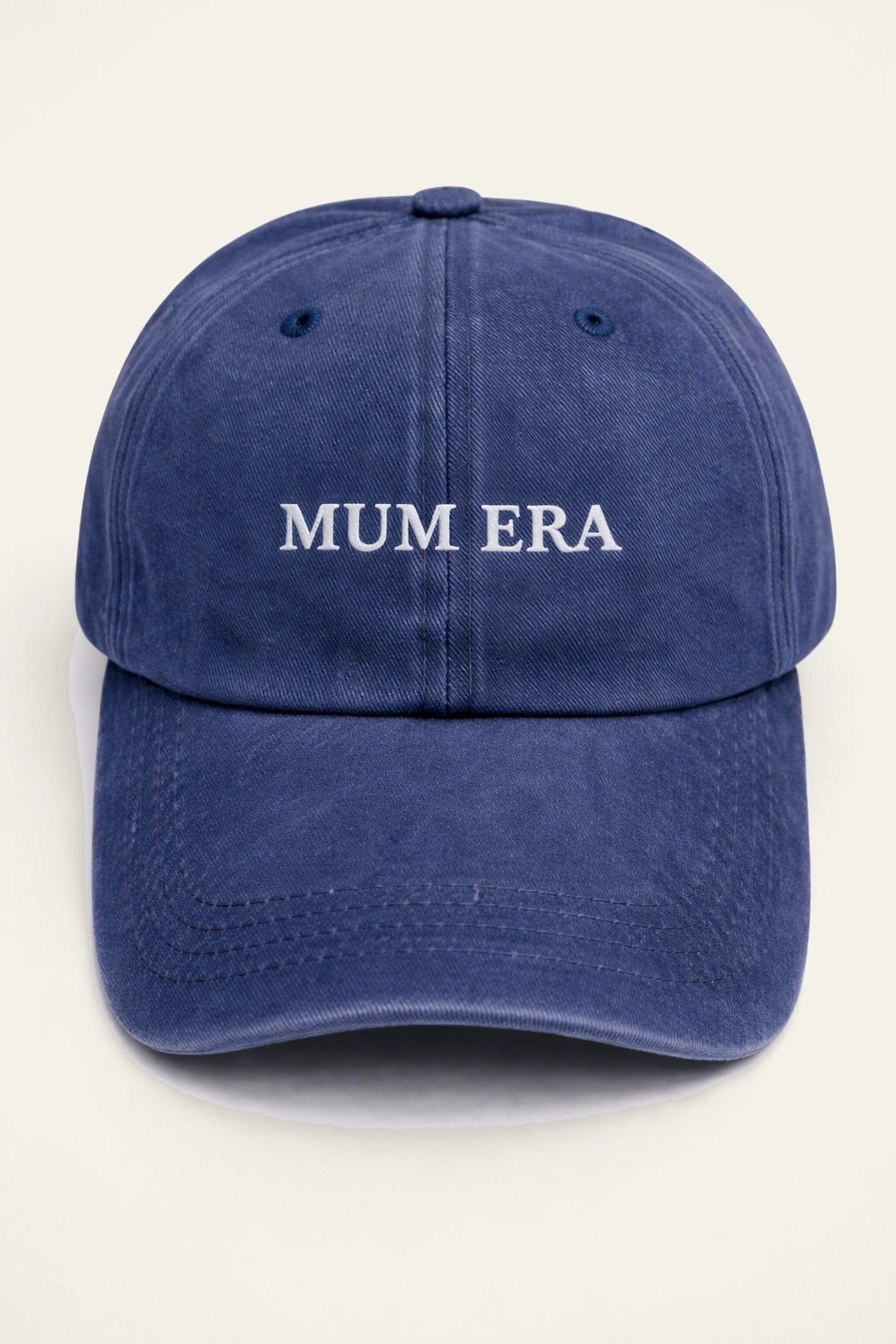 The Mum Era Cap in washed navy, worn outdoors, showing the white embroidered 'MUM ERA.' slogan.