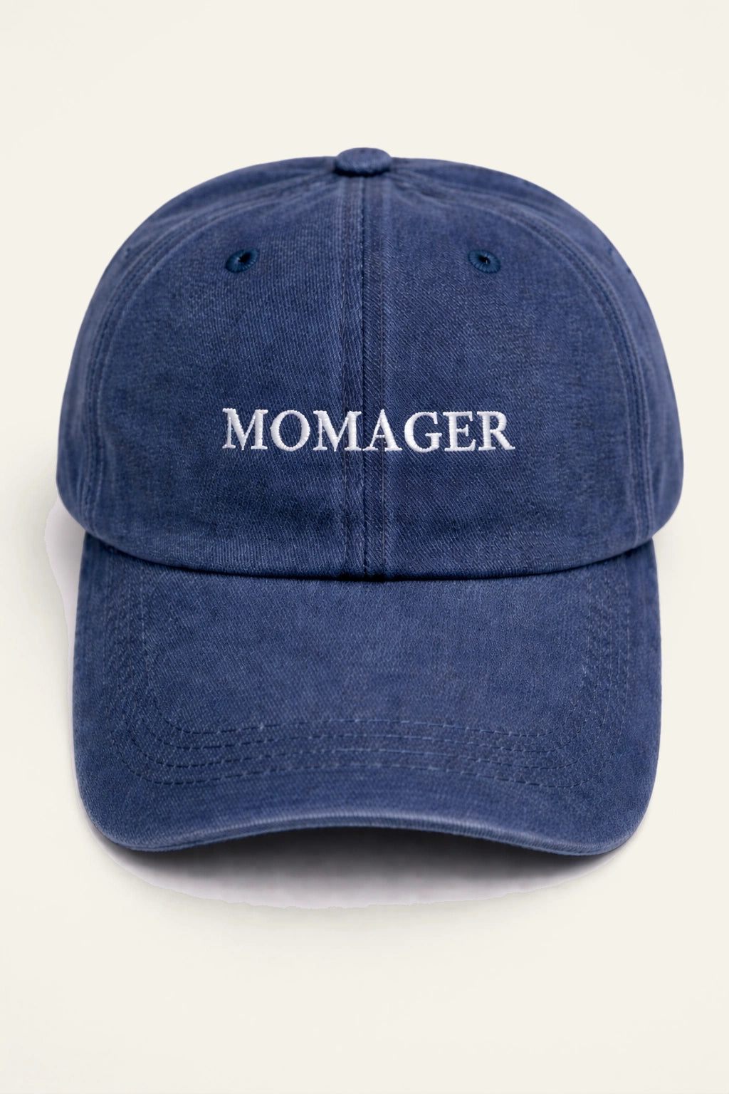 The Momager Cap in washed navy, worn outdoors, showing the white embroidered 'MOMAGER.' slogan.